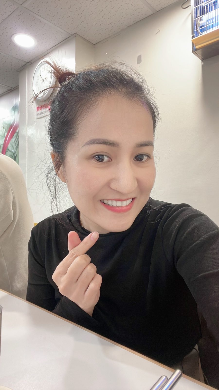 Xiao Cui smiling in her nail shop, making a small heart with her fingers