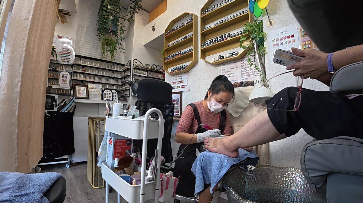 Xiao Cui giving a pedicure in her small shop with shelves of gel polish on the wall